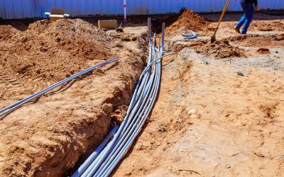 Trenched construction site with exposed pipes and scattered tools.