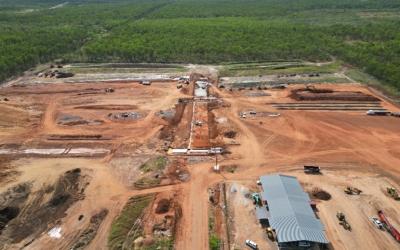 Construction site with earthworks and vehicles surrounded by dense green forest.